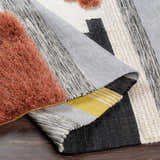 Close-up of the Elsenham Area Rug. Hand woven rug with black, brick red, cream, gray, and mustard colors. Bohemian style. Fold