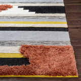 Close up of the Elsenham Area Rug with black, cream, gray, and mustard stripes and brick red shag detailing. Front