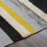 Close-up of the Elsenham Area Rug showing a striped pattern in black, gray, cream, and mustard on a wood floor. Texture