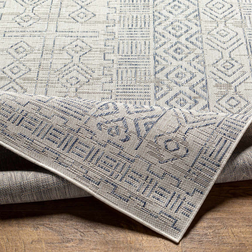 Close-up of the Epson Indoor & Outdoor Rug. Bohemian style rug with blue and gray geometric patterns. Machine woven polypropylene. Fold