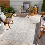 Outdoor patio scene with wood chairs and a blue and oatmeal Epson Indoor & Outdoor Rug. Roomscene-Rectangle