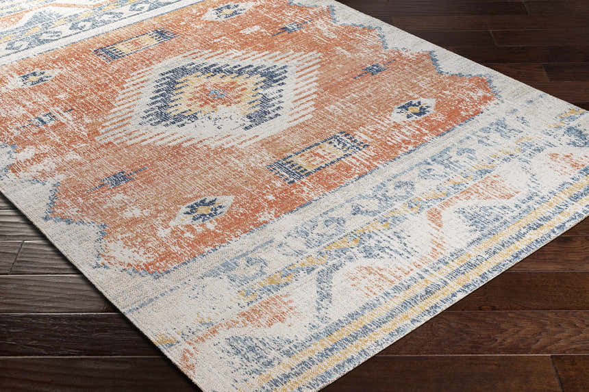 Close-up of the Etobicoke Area Rug showing its brick red, cream, and denim Southwestern-inspired pattern on dark wood floors. Corner