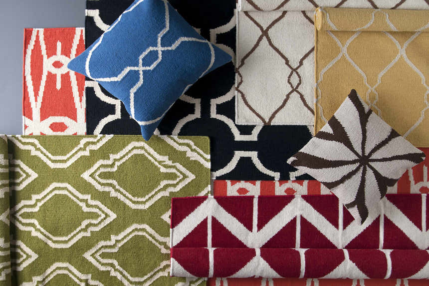 Close-up of Larimore Area Rug samples in olive, peach, black, and cream with geometric patterns and matching throw pillows. Styleshot