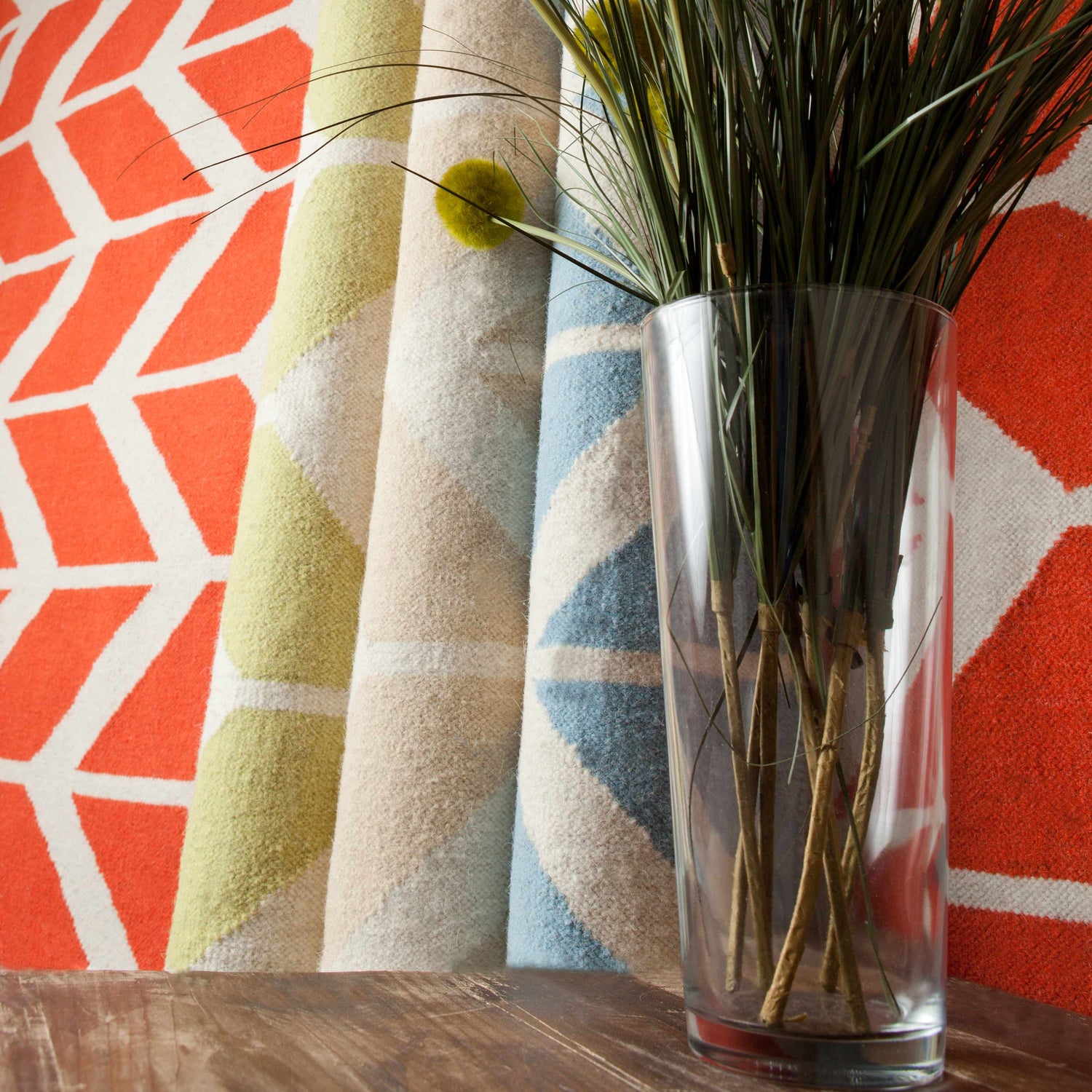 Rolled Elamton Area Rugs in beige, cream, and blue with a geometric pattern and a vase of greenery. Styleshot