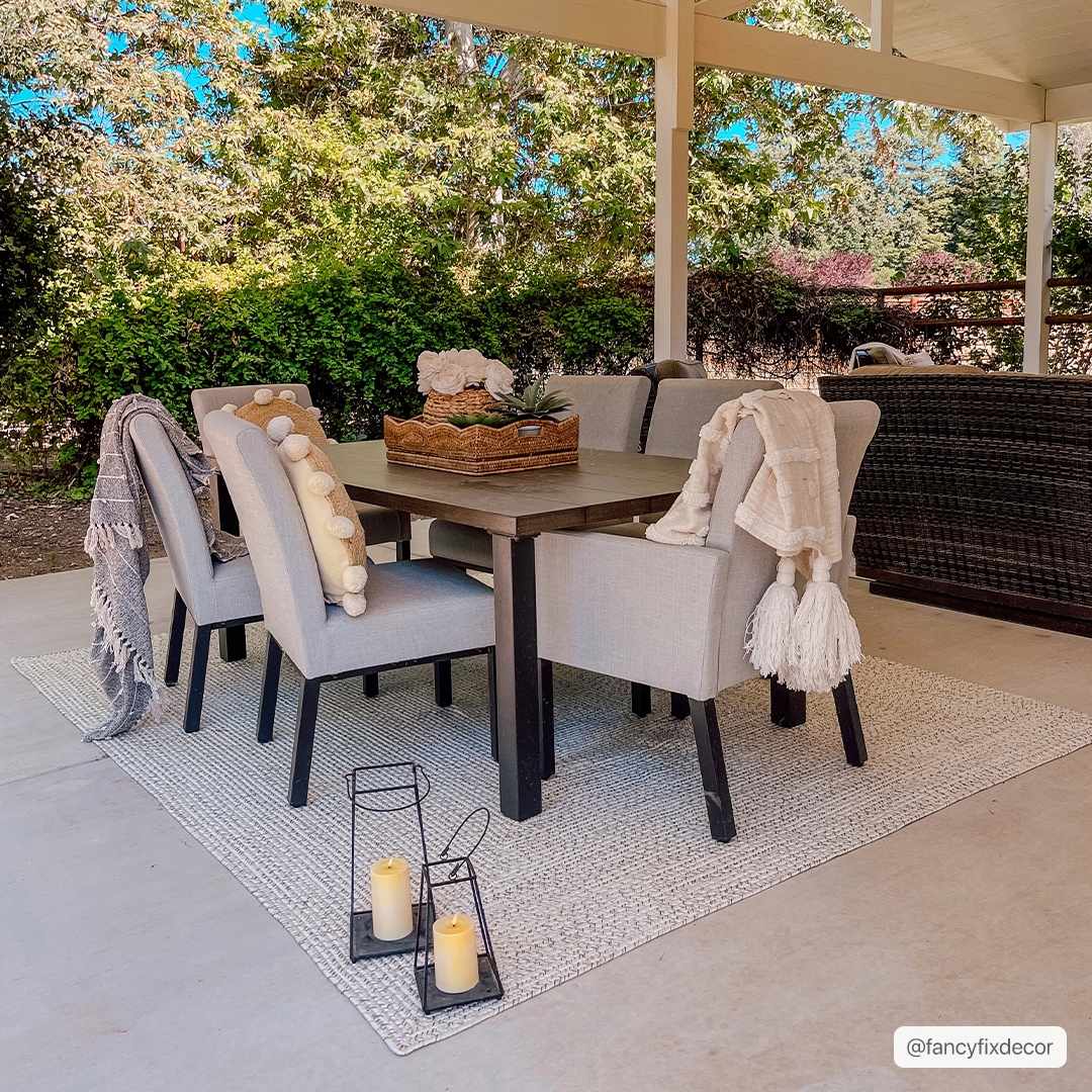 Outdoor dining area with a Beige Braided Faux Jute Rug under a table and chairs. Neutral tones and natural light. Roomscene-Rectangle