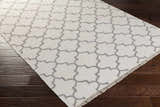 Close-up of Fellsmere Area Rug, charcoal quatrefoil pattern on ivory wool, with fringe, on dark wood floor. Corner