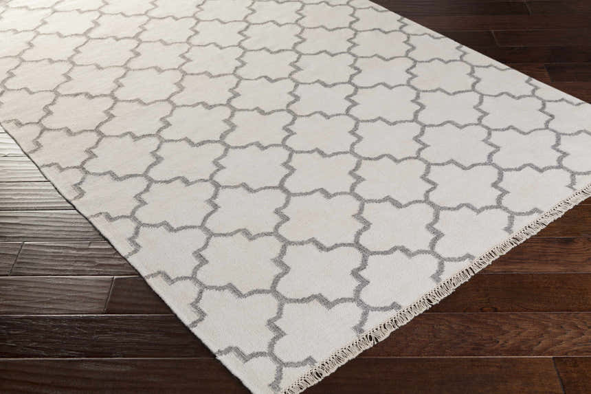 Close-up of Fellsmere Area Rug, charcoal quatrefoil pattern on ivory wool, with fringe, on dark wood floor. Corner