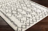 Close-up of the Fenstanton Area Rug. Cream shag rug with a charcoal geometric pattern on dark wood floors. Corner