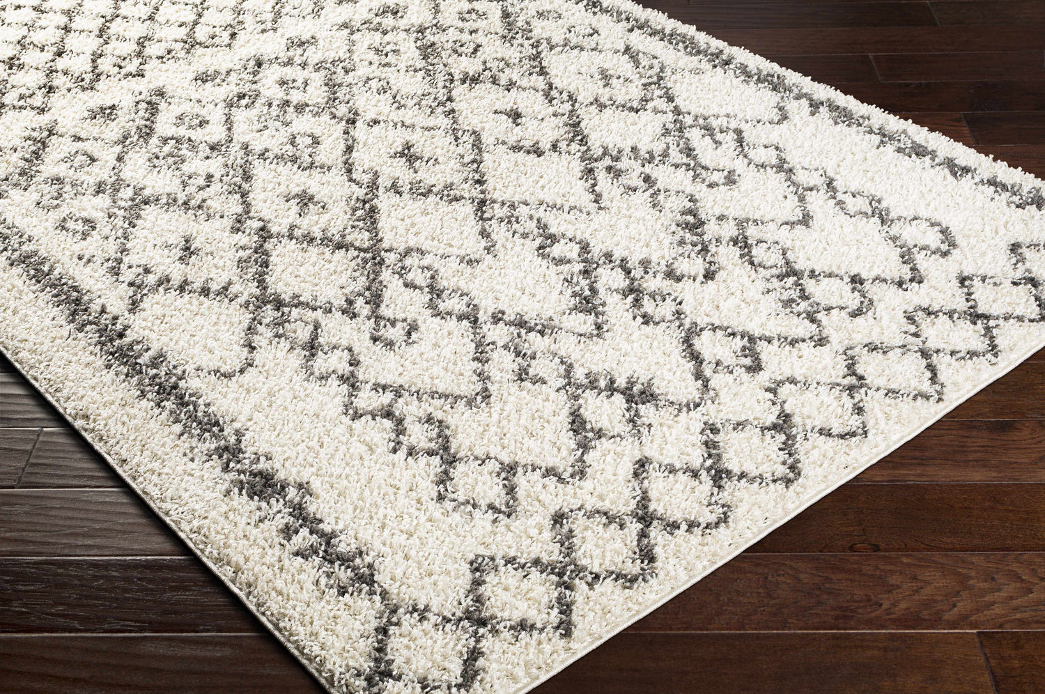 Close-up of the Fenstanton Area Rug. Cream shag rug with a charcoal geometric pattern on dark wood floors. Corner