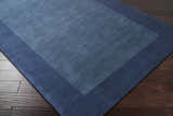 Close-up of a Bordered Solid Ink Blue Wool Rug showing texture and border detail on dark wood flooring. Corner