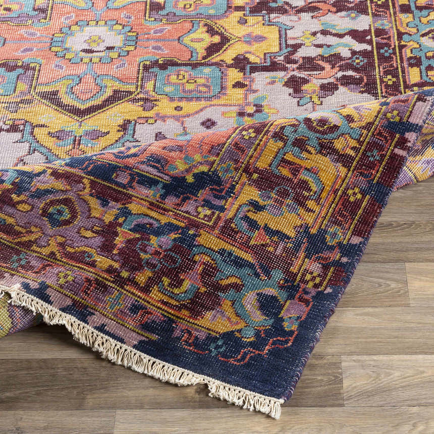 Close-up of the hand-knotted Flagtown Area Rug. Features a traditional, vintage design with blue, coral, and purple tones. Fold