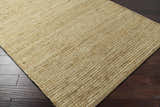 Close-up of the Frederic Jute Carpet showing its tan color, hand woven texture, and rectangular shape on dark wood flooring. Corner