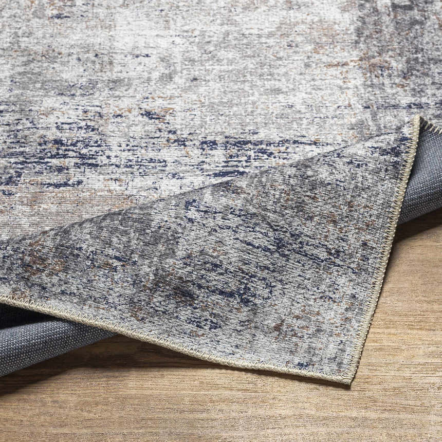 Close-up of the Fairplains Washable Area Rug. Features a distressed vintage pattern in charcoal, navy, gray, and brown tones. Fold
