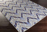 Close-up of Fryeburg Area Rug: hand-woven wool rug with beige ground and lavender chevron pattern on dark wood floor. Corner