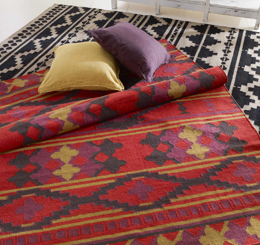 Styled Gratiot Area Rug. Hand woven rug in black, gray, red, purple, and gold with geometric patterns. Pillows add texture. Styleshot