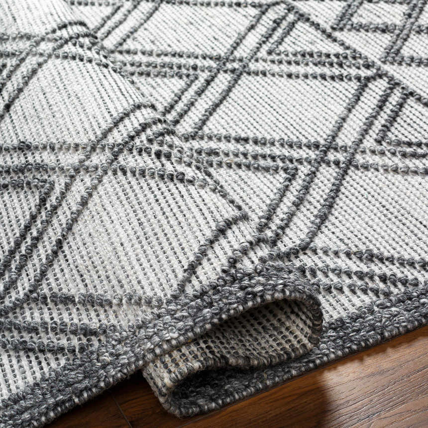 Close-up of the Gada Area Rug. Hand woven texture with a geometric dark gray and light gray pattern. Farmhouse style. Fold
