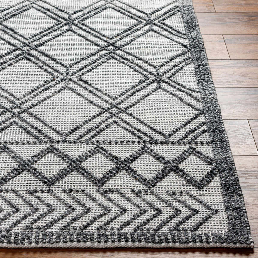 Close-up of the Gada Area Rug, showing its dark gray geometric pattern and hand-woven texture on a light gray base. Front