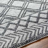 Close-up of the Gada Area Rug showing its dark gray geometric pattern on a light gray, hand-woven texture. Texture