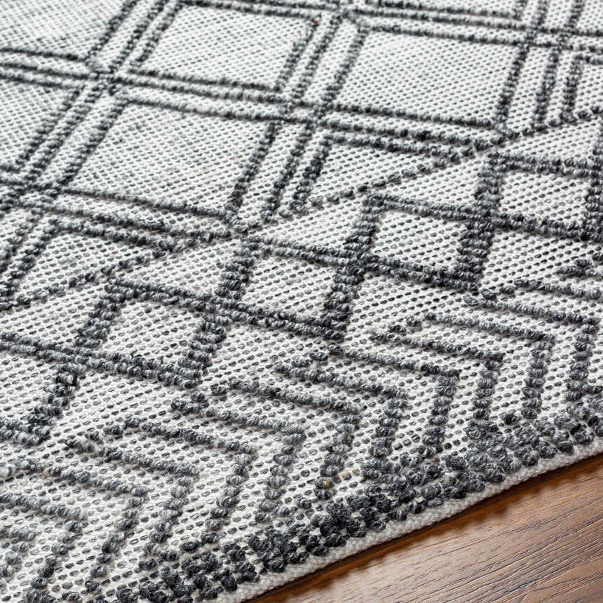 Close-up of the Gada Area Rug showing its dark gray geometric pattern on a light gray, hand-woven texture. Texture