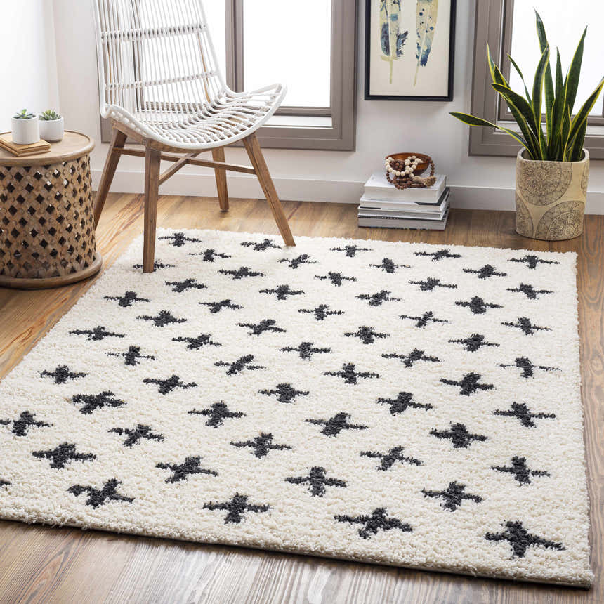 Living room scene with a white wicker chair on a Gambo Area Rug with black cross pattern. Roomscene-Rectangle