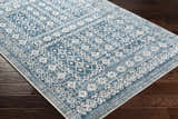 Close-up of the Gandy Washable Area Rug. Features a blue and cream geometric pattern on a dark wood floor. Corner
