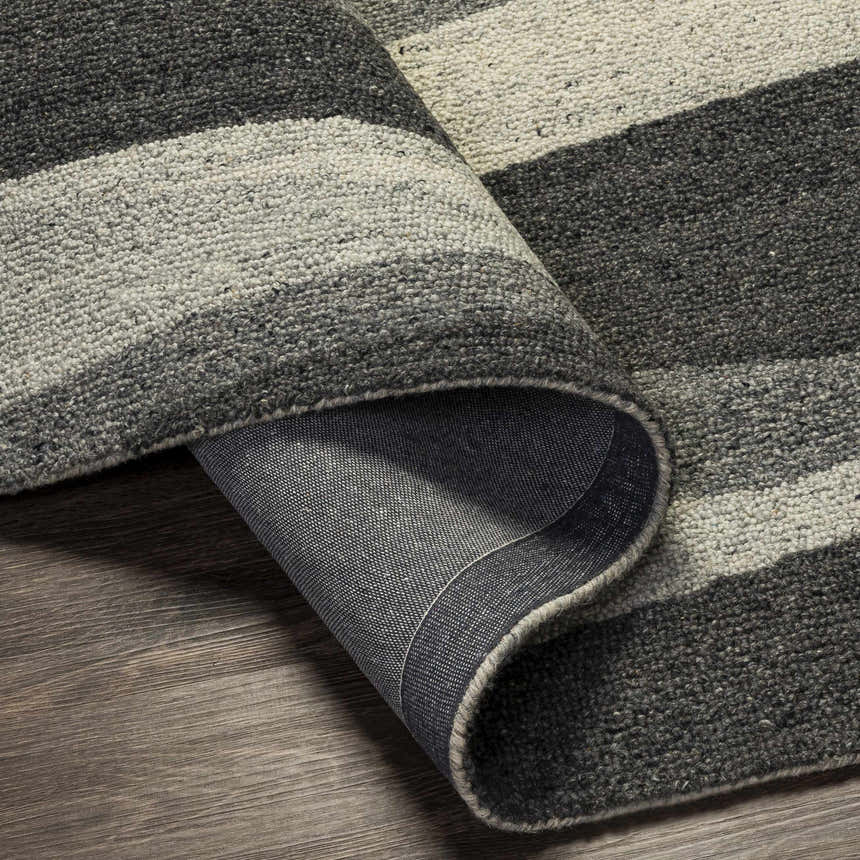 Close-up of the hand-tufted Garlands Area Rug. Wool rug with black, charcoal, and gray stripes on a wood floor. Fold