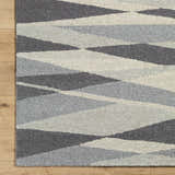 Close-up of the hand-tufted Garlands Area Rug. Wool rug features a contemporary geometric pattern in black, charcoal, gray, and light gray. Corner
