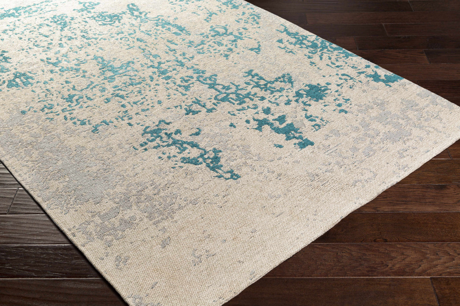 Close-up of Sweeny Beige/Blue Abstract Area Rug on dark wood floor. Beige rug with teal and slate abstract pattern. Corner