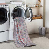 Laundry room scene with a Rust Goma Vintage Area Rug partially inside a dryer. The rug has blush, red, and blue tones. Washing-Machine