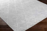 Close-up of the light gray Gonvick Area Rug showing its hand-knotted texture and off-white geometric diamond pattern. Corner