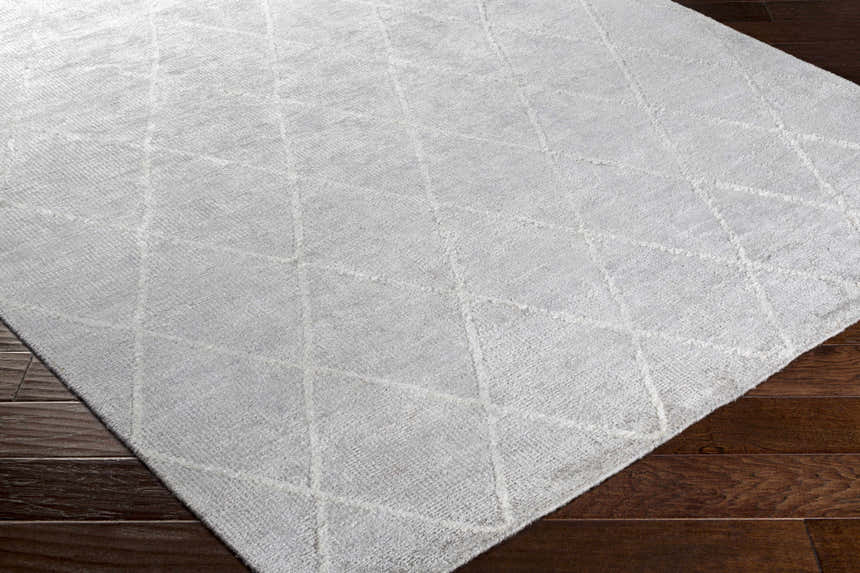 Close-up of the light gray Gonvick Area Rug showing its hand-knotted texture and off-white geometric diamond pattern. Corner