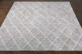 Close-up of the Gonvick Area Rug. Light gray viscose rug with an off-white geometric diamond pattern. Hand-knotted texture. Front