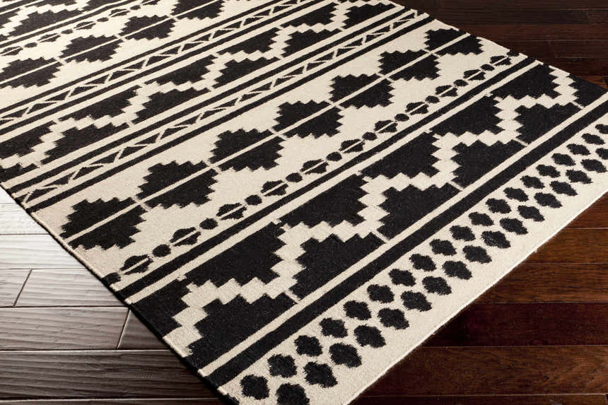 Close-up of the hand woven Gratiot Area Rug. Black geometric patterns on a medium gray background. Bathroom, kitchen, mudroom rug. Corner