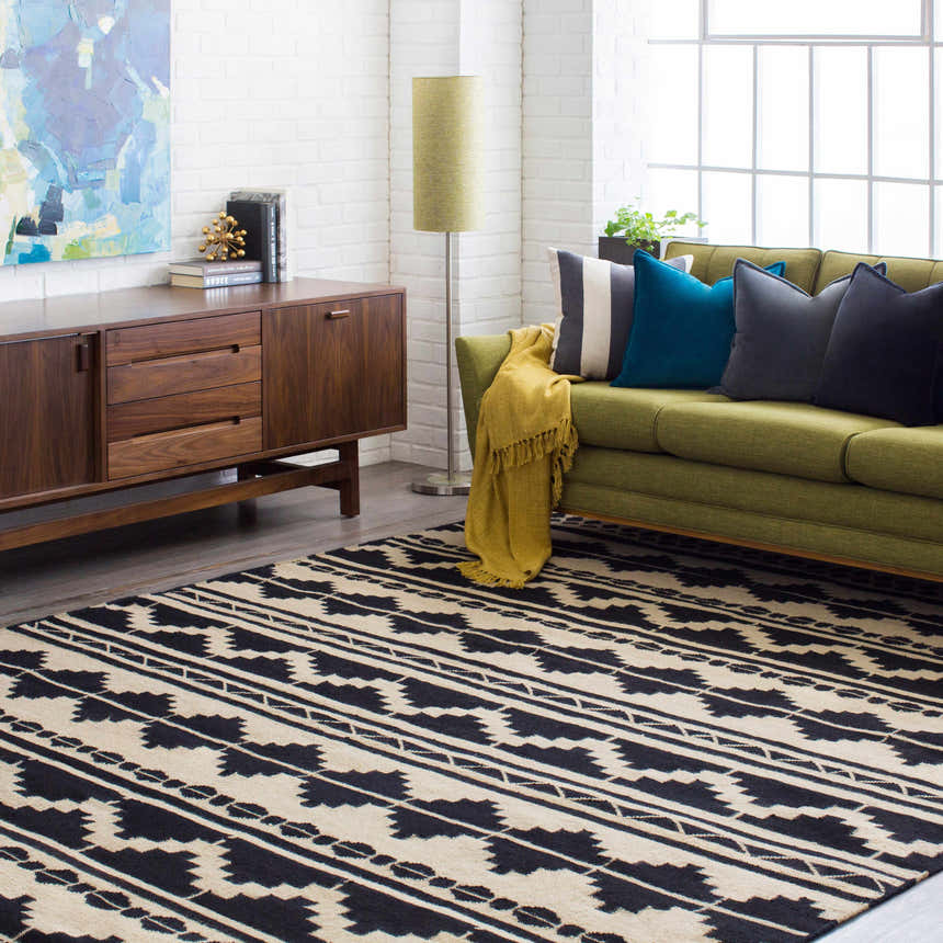 Living room scene with black and gray Gratiot Area Rug, green sofa, wood cabinet, and white brick wall. Roomscene-Rectangle