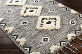 Close-up of the Gardner Cream on Gray Wool Tassel Rug. Features geometric patterns and cream-colored tassels on a hand-woven wool rug. Corner