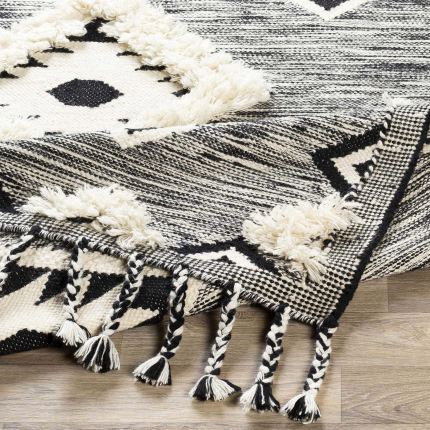 Close-up of the hand woven Gardner Cream on Gray Wool Tassel Rug, featuring black and cream geometric patterns and braided tassels. Fold
