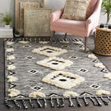 Bohemian living room scene with a Gardner Cream on Gray Wool Tassel Rug, pink chair, and eclectic decor. Roomscene-Rectangle