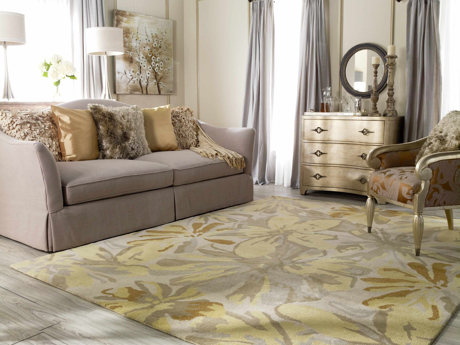 Living room scene with floral Grindstone Area Rug in light gray, olive, tan, and wheat tones. Sofa, chair, and dresser are visible. Roomscene-Rectangle