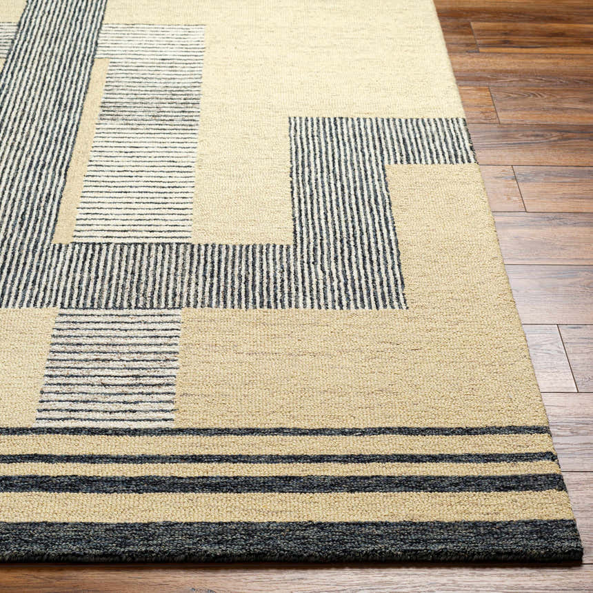 Close-up of the Guta Area Rug showing a geometric pattern in beige and black on a hardwood floor. Hand-tufted wool texture. Front
