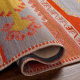 Close-up of the hand-woven Gumberry Area Rug. Features brick red, mustard, and navy hues in a contemporary Southwestern pattern. Fold