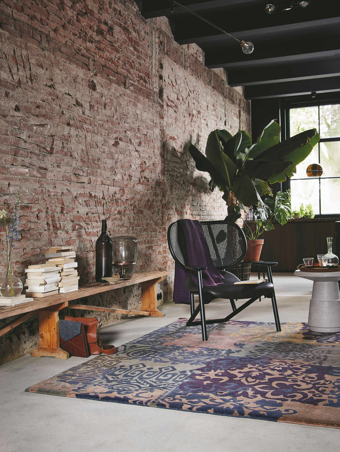 Loft living room with brick wall, Hallsboro Area Rug in charcoal, brown, gray, and a black chair. Contemporary style. Roomscene-Rectangle