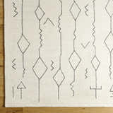 Close up of the hand tufted Hanny Area Rug. Beige wool rug with black geometric shapes. Corner