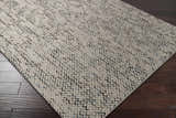 Close-up of the hand woven Hansell Area Rug. Ivory wool rug with charcoal and ice blue accents. Contemporary, natural fibers style. Corner