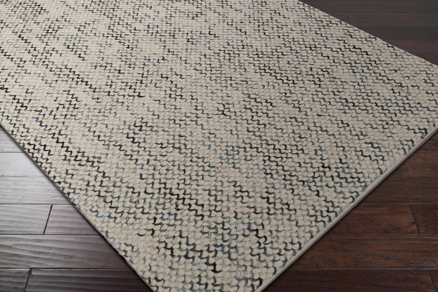 Close-up of the hand woven Hansell Area Rug. Ivory wool rug with charcoal and ice blue accents. Contemporary, natural fibers style. Corner