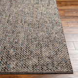 Close up of the hand woven Hansell Area Rug showing charcoal, ivory, and blue tones on wood floor. Front