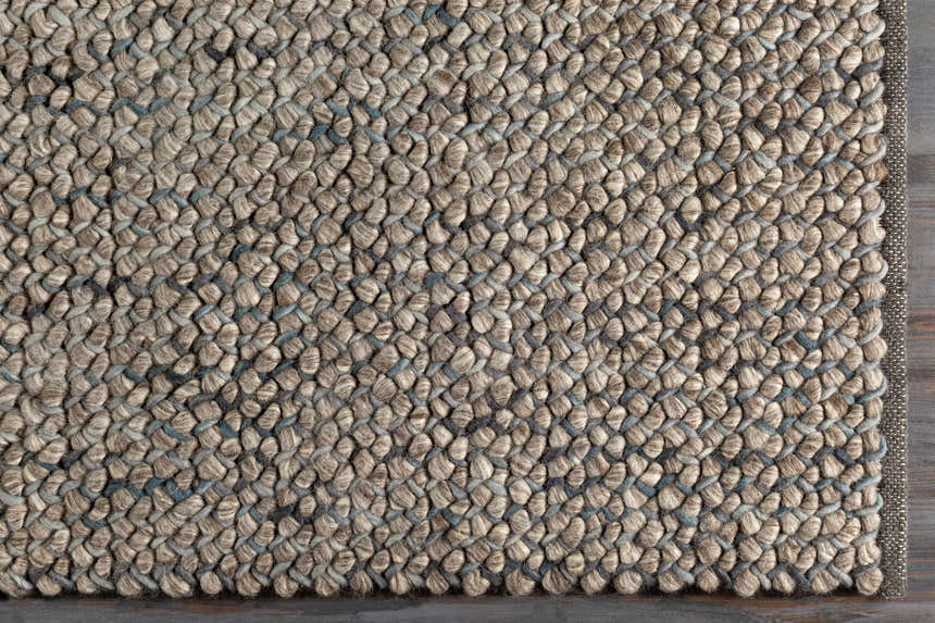 Close-up of the hand woven Hansell Area Rug. Charcoal, ivory, and ice blue wool rug with a textured, contemporary design. Corner