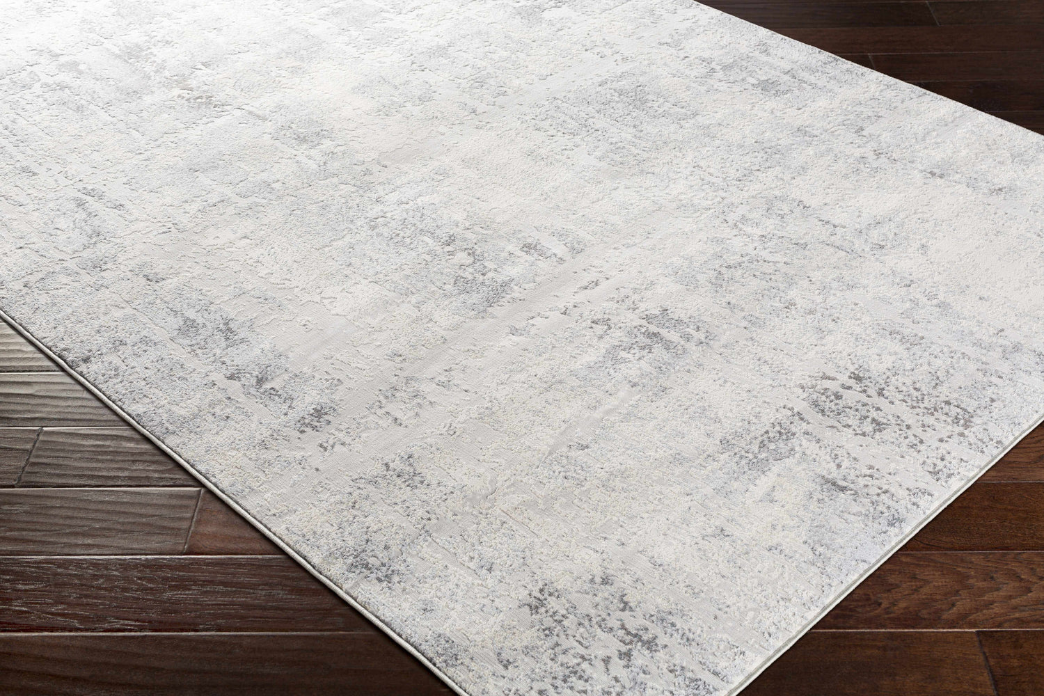 Close-up of the Hardeeville Area Rug, a light gray rug with a subtle, distressed pattern on dark wood flooring. Corner