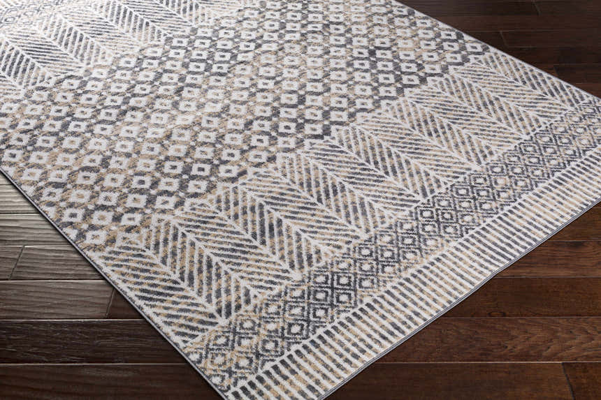 Close-up of Hassocks Area Rug: charcoal, cream, light gray, and tan geometric pattern on dark wood floor. Corner