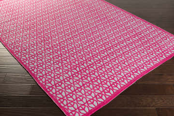 Close-up of the Heppner Area Rug showing a geometric fuchsia and light sage pattern on a dark wood floor. Corner