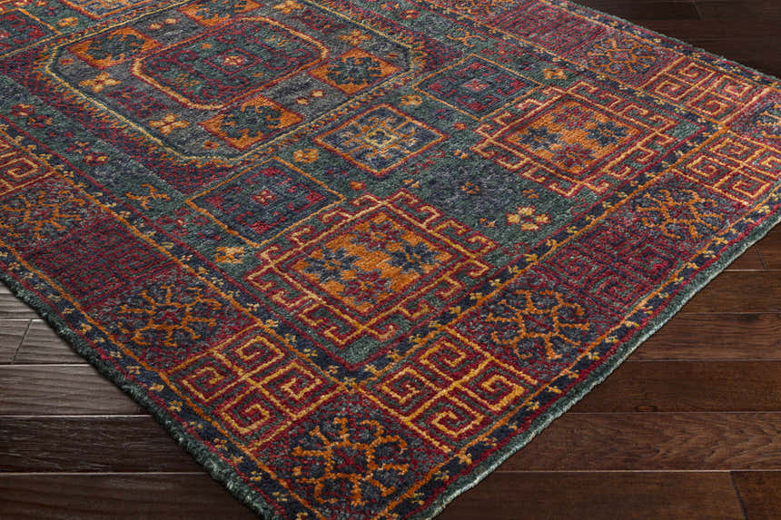 Close up of the hand knotted Herman Jute Carpet. Features burnt orange, dark green, mustard, navy, and red colors. Corner